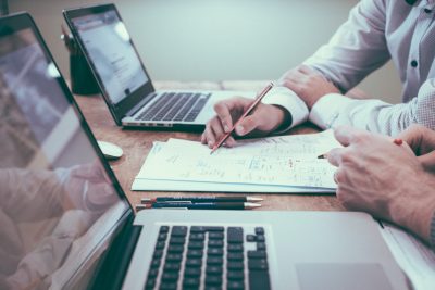 Aufgeklappte Notebooks, davor sichtbare Hände, die etwas notieren